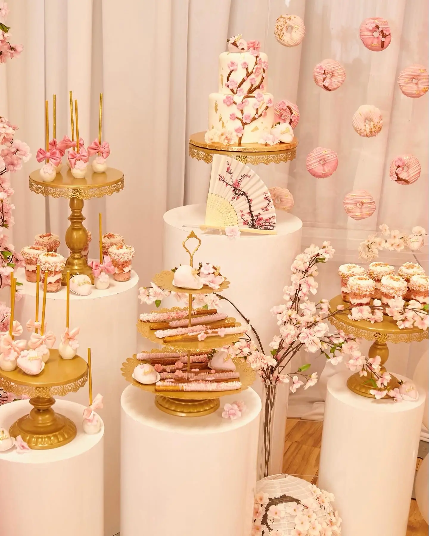 Luxury cherry blossom dessert table with gold cake stands, cupcakes, and blush décor for an elegant celebration.