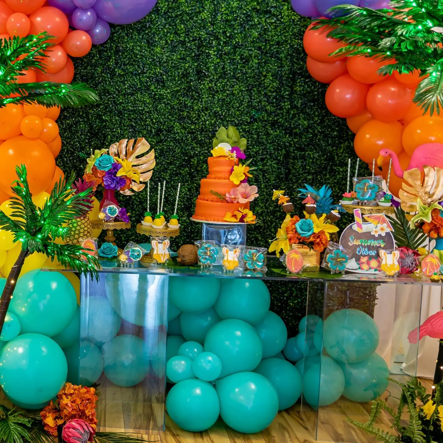 Vibrant tropical themed baby shower setup featuring colorful balloon wall and themed decorations.