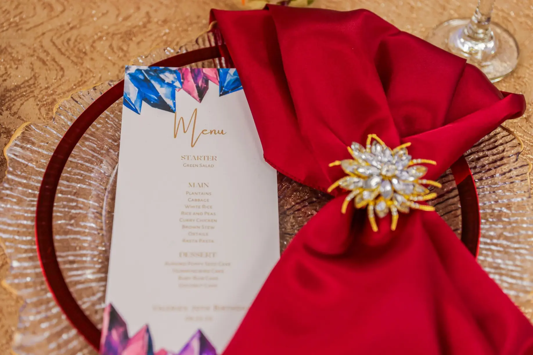 Close-up of elegant red napkin and gold brooch/napkin ring detail from a luxury table setting.