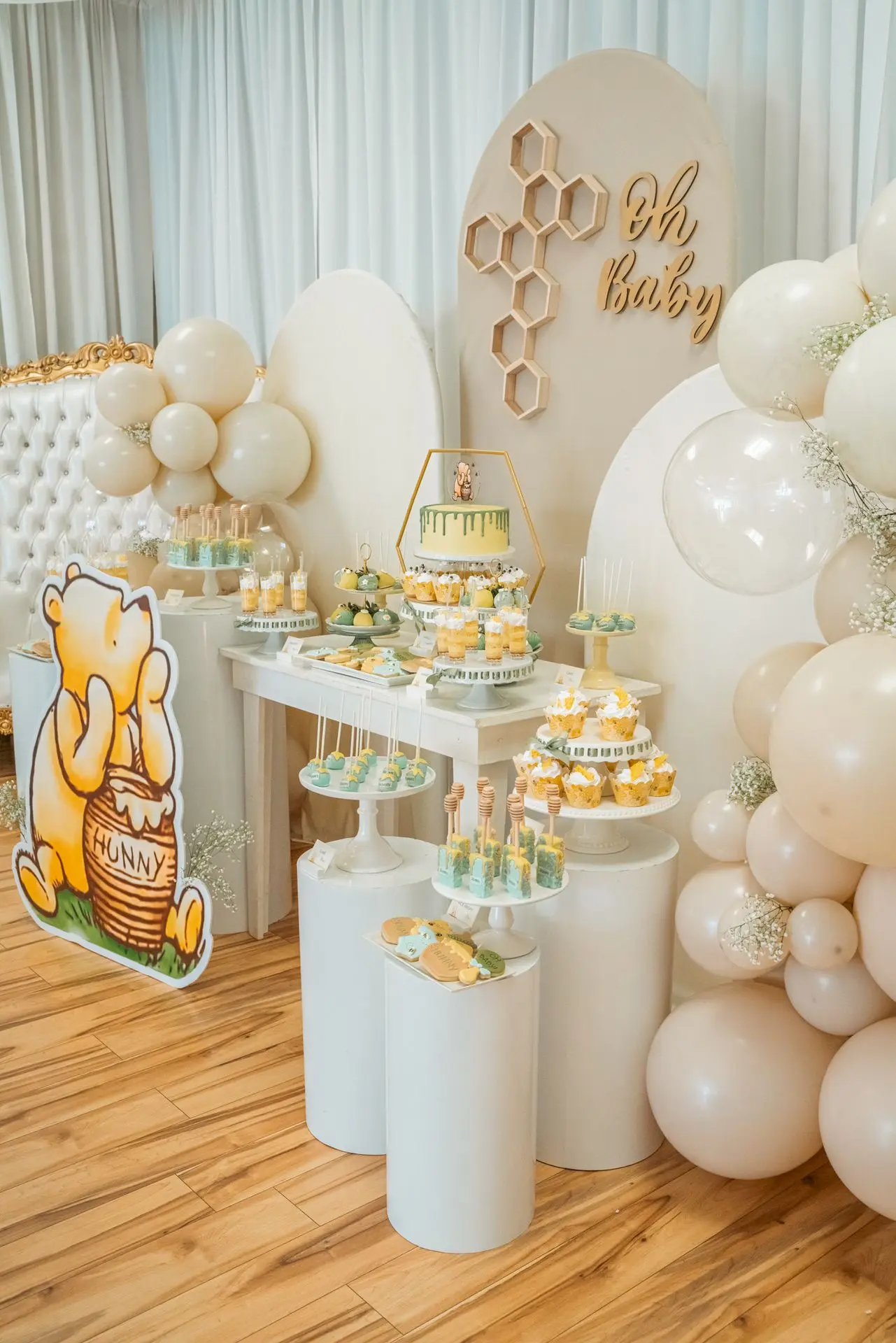 Neutral baby shower setup with white balloon arch, winnie the pooh décor, and babies breathe flowers