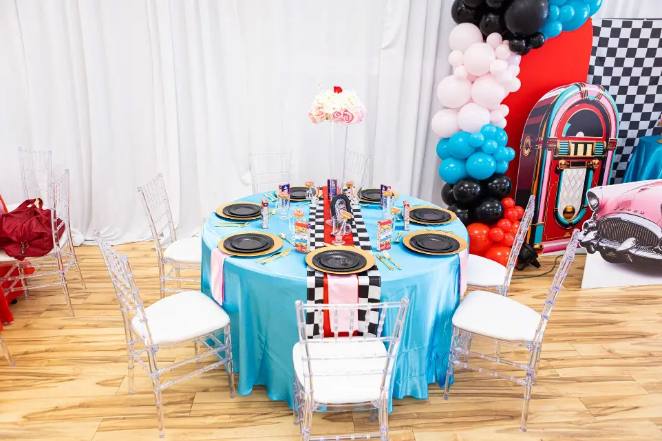 Whimsical birthday setup with blue, pink, and red balloon décor and themed cake display. Sock hop, Grease, Soda Shop Theme